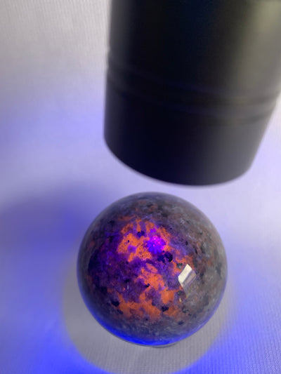 Close-up of  yooperlite sphere with colorful interior patterns under a black light.